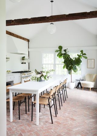 White kitchen with brick paved floor and white dining table with woven chairs