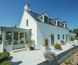 white house with dormer windows in roof and green orangery to side