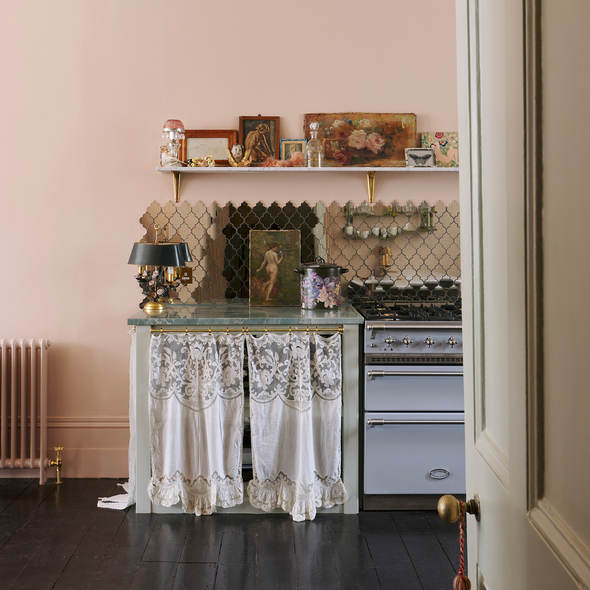 kitchen with pink walls and dark wood floors blue range cooker and mirrored splashback with open shelves dressed with vintage decor and grey cabinetry with lace front devol