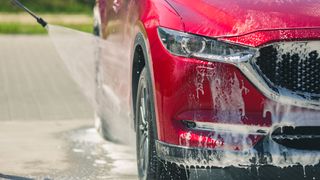 A red car being cleaned with a pressure washer