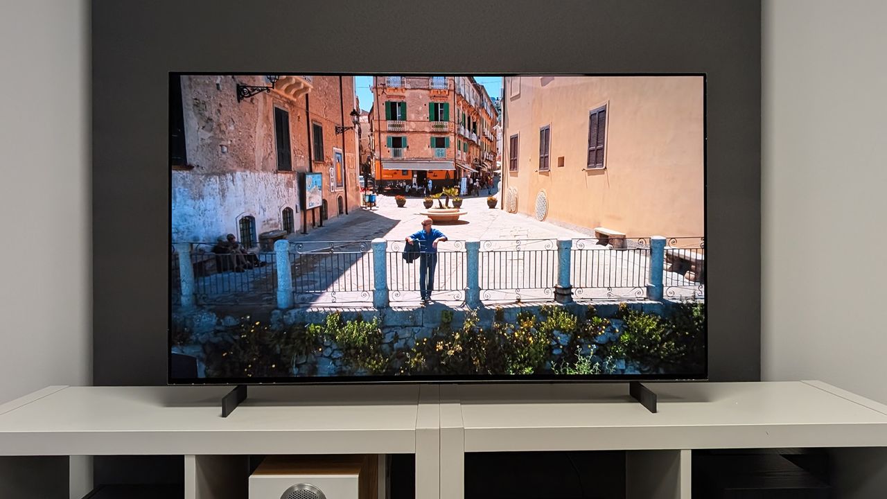 The LG C5 42-inch OLED TV seen straight-on on a TV cabinet. On screen is Stanley Tucci looking out over some railings in a picturesque Italian town.
