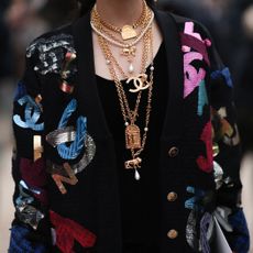 Guest outside of Chanel show wearing a black Chanel cardigan and lots of Chanel necklaces