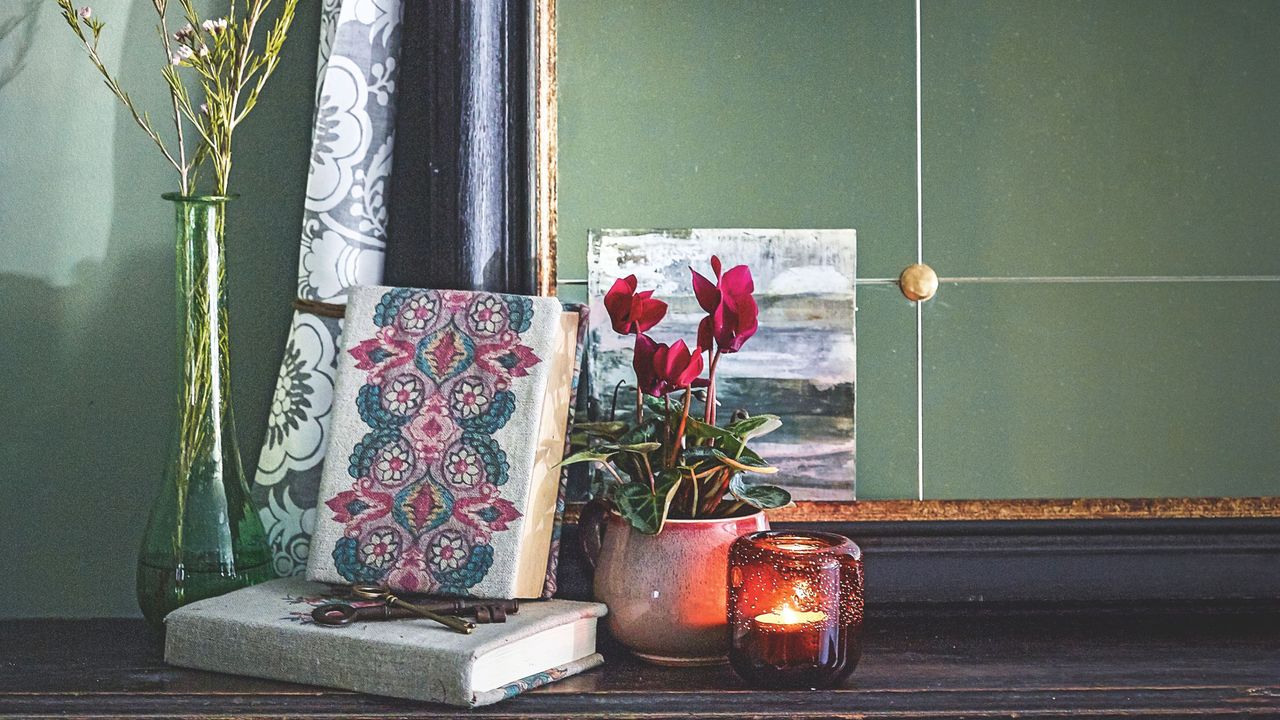 Red-pink flowering cyclamen plant in front of mirror next to books in bedroom