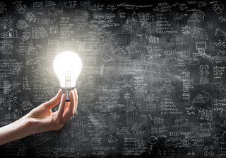 A hand holding a lit lightbulb against scribbles on a blackboard