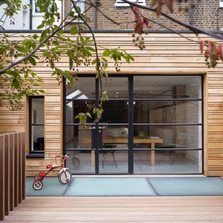 Exterior of house with glass and steel doors leading onto glass and wood decking area