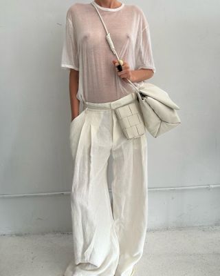 A sheer white T-shirt worn with white trousers and two white bags.