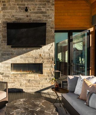 fall outdoor living, porch with outdoor tv, couch, coffee table, armchair, modern fire place in brick wall, view of interior