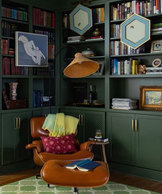 corner of room with dark green cabinetry with books displayed and tan leather chair