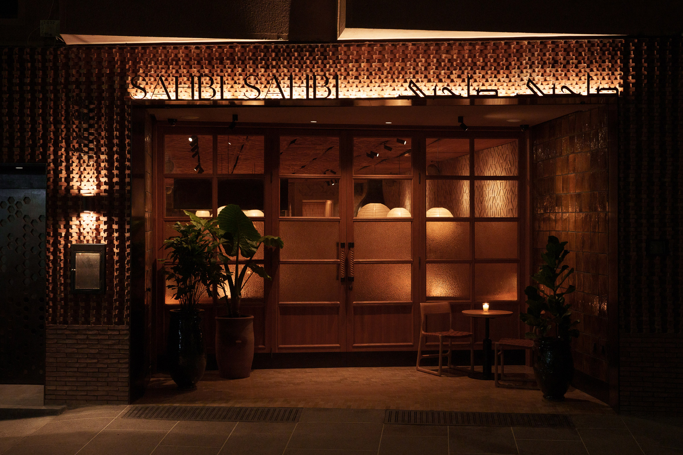 The facade of a restaurant is captured at night as its terracotta tones are brought to life by diffused, warm lantern lights and back-lit signs.