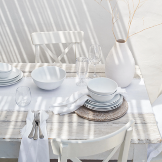 White dinnerware stacked on top of rattan placemat on dining table