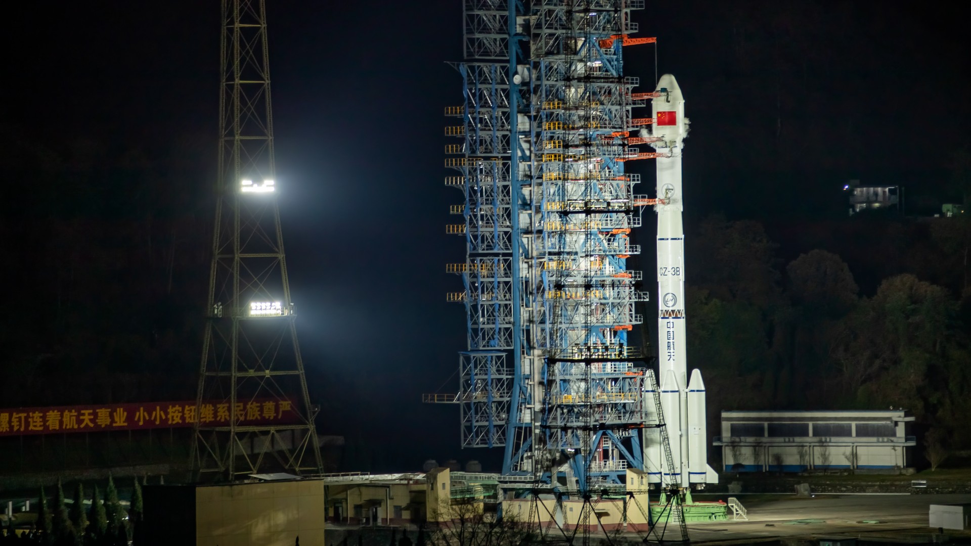 a white rocket stands upright on a launch pad, illuminated by flood lights at night
