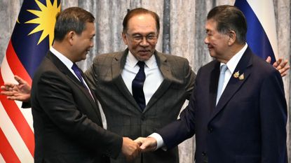Cambodia's Prime Minister Hun Manet and Thailand's acting Prime Minister Phumtham Wechayachai shake hands as Malaysia's Prime Minister Anwar Ibrahim puts his arms around them following a press conference announcing ceasefire
