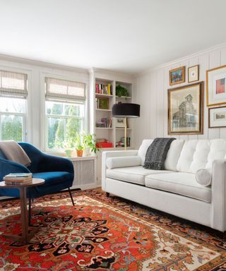 living room with white sofa, neutral panelled walls, large red vintage rug and teal accent chair