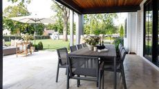 Outdoor dining area with an 8-seat table and a large tiled patio area with outdoor lounge furniture. There is a lawn area visible in the background