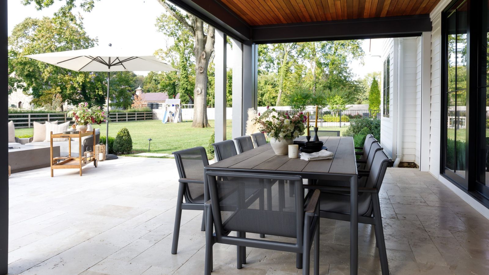 Outdoor dining area with an 8-seat table and a large tiled patio area with outdoor lounge furniture. There is a lawn area visible in the background