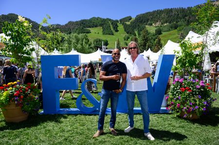 Darius Rucker and Chris Radomski standing in front of a big blue sign saying 'F&W' with white tents and green hills in the background