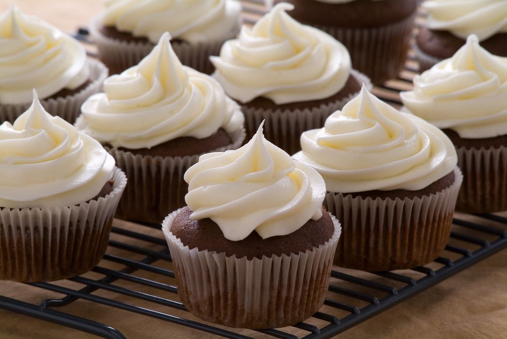 Chocolate cupcakes with cream cheese frosting sit on a baking rack.