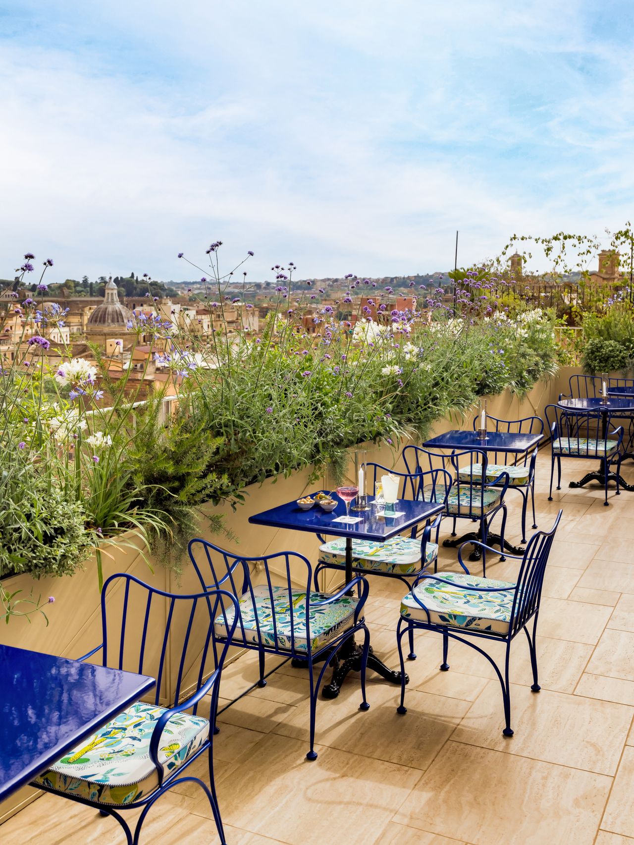 The terrace of a hotel is filled with plants and Art Deco-inspired blue and floral furniture.