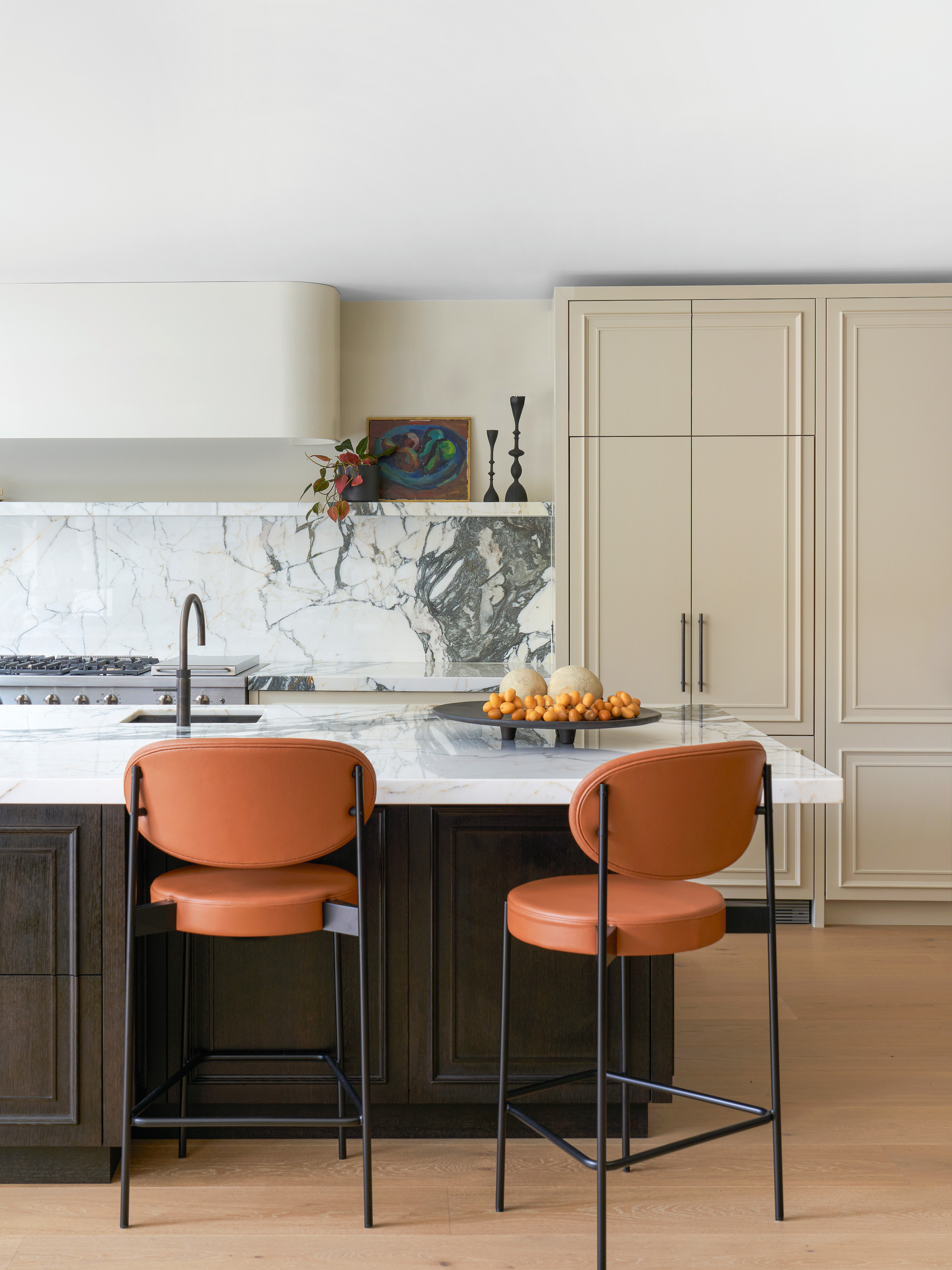 Kitchen with cream and dark brown Shaker-style units, orange bar stools and white marble countertops