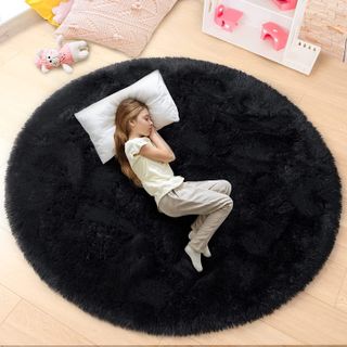 A child sleeps on a large circular black rug.