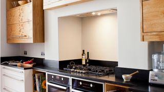 A cream kitchen with black countertops and black oven showing task lights overhead