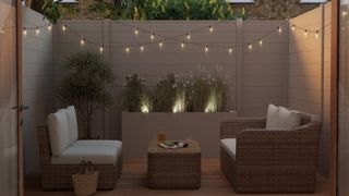 A small garden with outdoor sofa and festoon lights hung on a light coloured fence