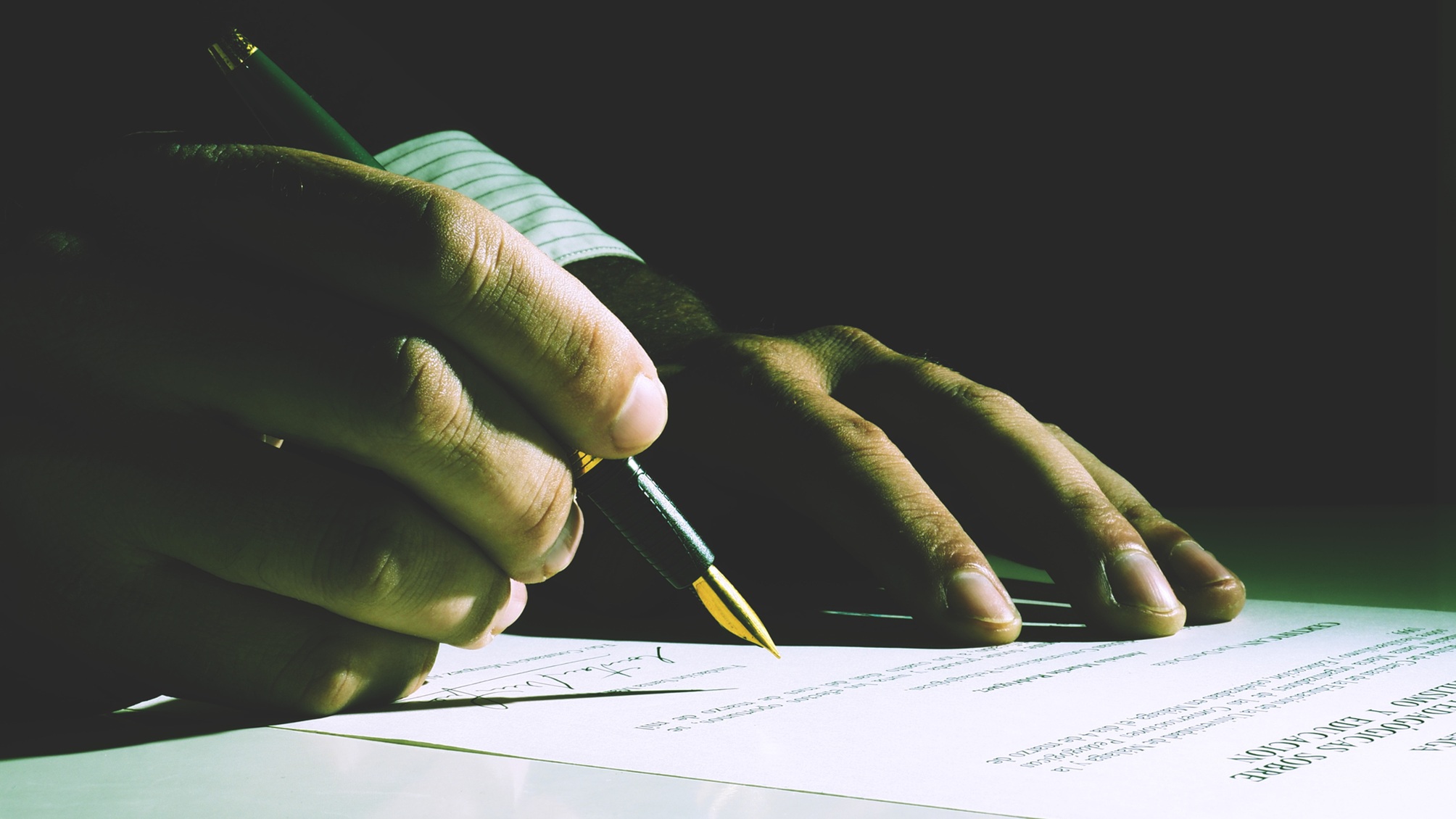 A man signs paperwork, only his hands showing.