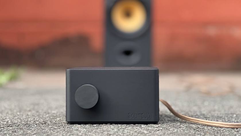 The SoundUp portable Bluetooth amplifier outside on concrete with a speaker blurred but visible in the background