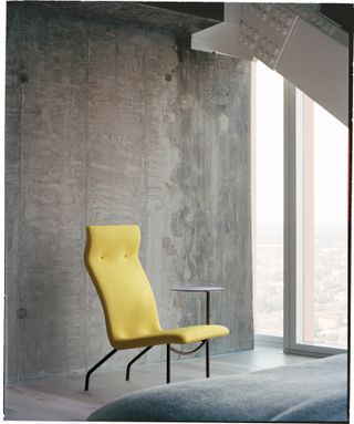 Citrus coloured 'Lucio’ lounge chair and side table against a grey wall by a window