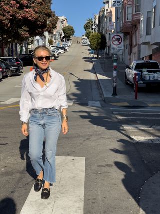 Woman wearing a white button-down and jeans with black Gucci loafers.