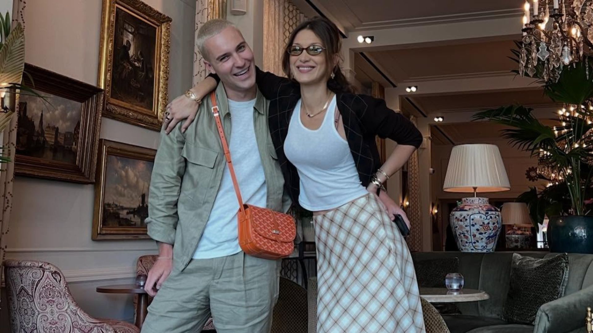 Bella Hadid poses with a friend wearing a knee-length skirt with knee-high boots with a tank-top and cardigan.