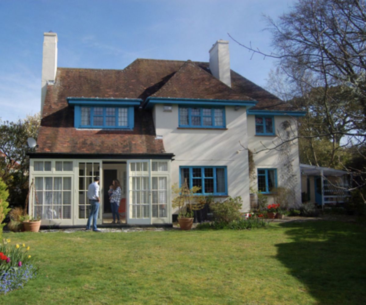 The before shot of a detached home with blue window frames and drainpipes before a new extension is added