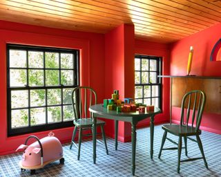 Play area with red walls, wooden ceiling, green table and chairs and checked carpet