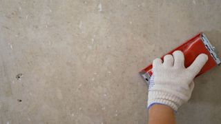 A wall being sanded down by hand. The hand holding the sanding block is wearing a white fabric glove.
