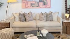 cream soho home sofa styled with cushions under a large artwork next to timber side tables, a floor lamp, round stone coffee table with diffuser and lamp and book