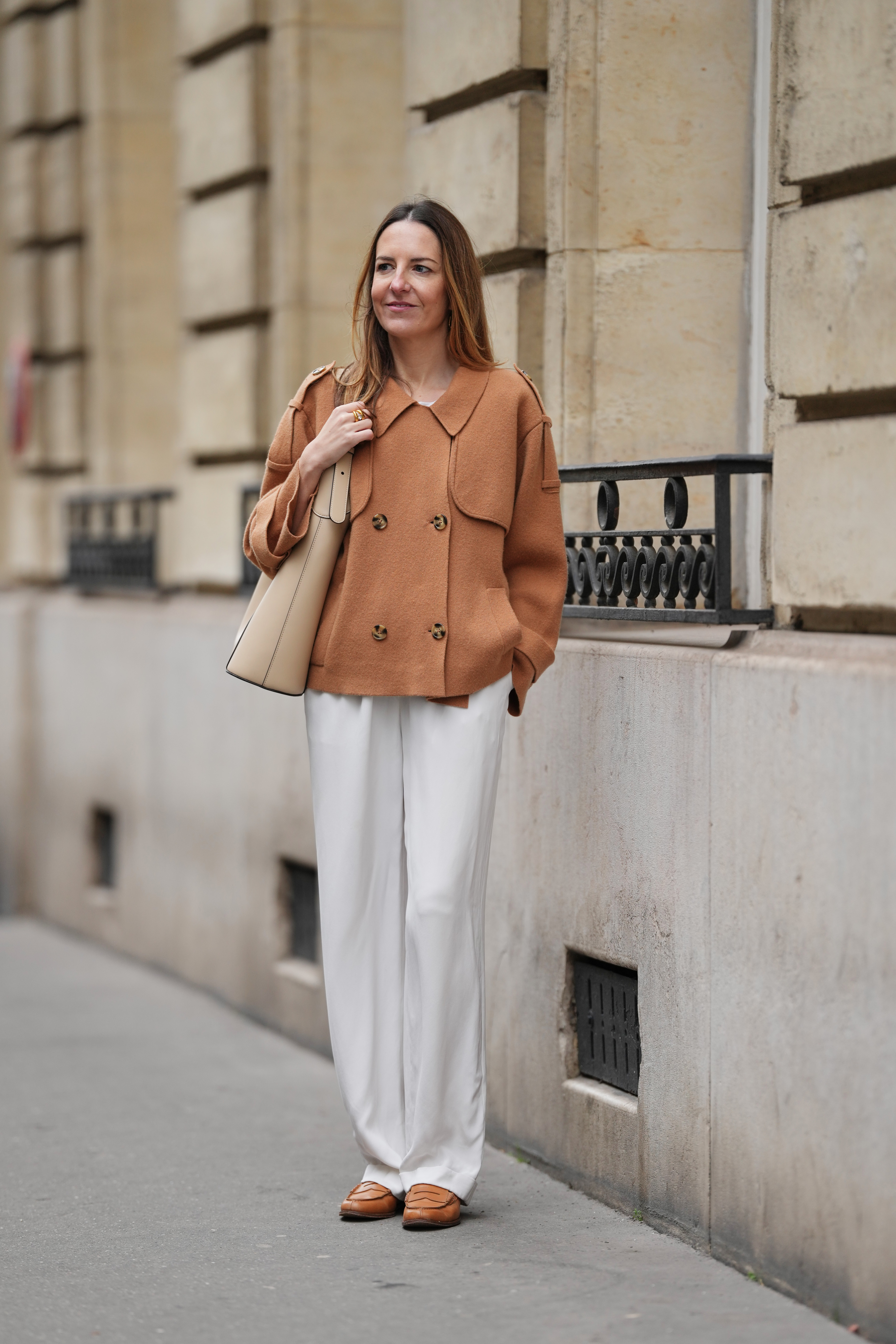 PARIS, FRANCE - JANUARY 15: Alba Garavito Torre wears long light brown hair worn loose and parted at the side, gold-tone jewelry by Sempiterno Paris, a brown pea coat with a double-breasted front and notched lapels, white silk straight-leg pants with a fluid drape, camel leather loafers shoes by Church&amp;rsquo;s with a rounded toe and low heel, and a beige smooth calf-leather hobo bag with a sculptural curved shape by Studio Flo carried on the shoulder, during a street style fashion photo session, on January 15, 2026 in Paris, France. (Photo by Edward Berthelot/Getty Images)