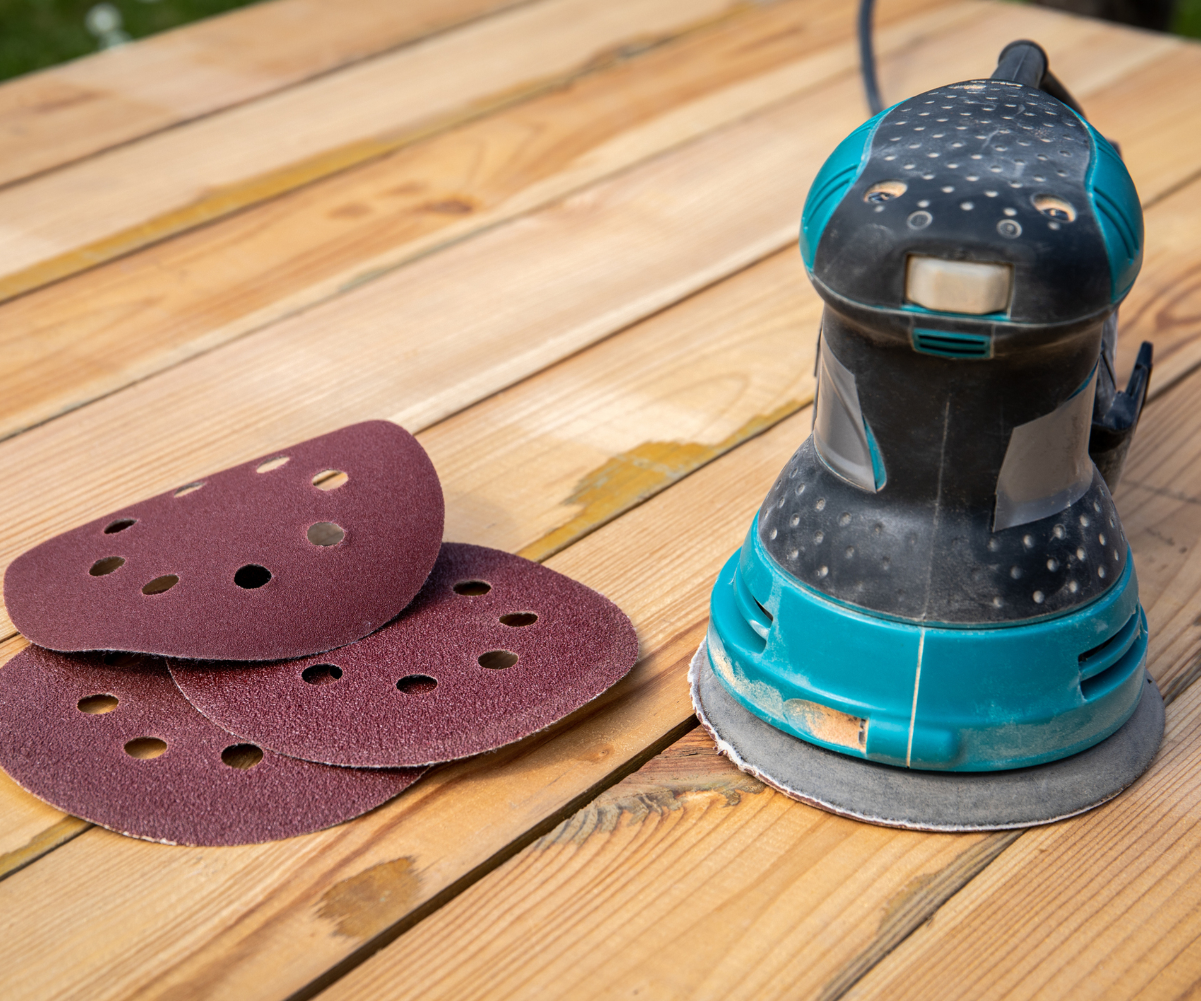 orbital sander and sanding sheets on planks of wood