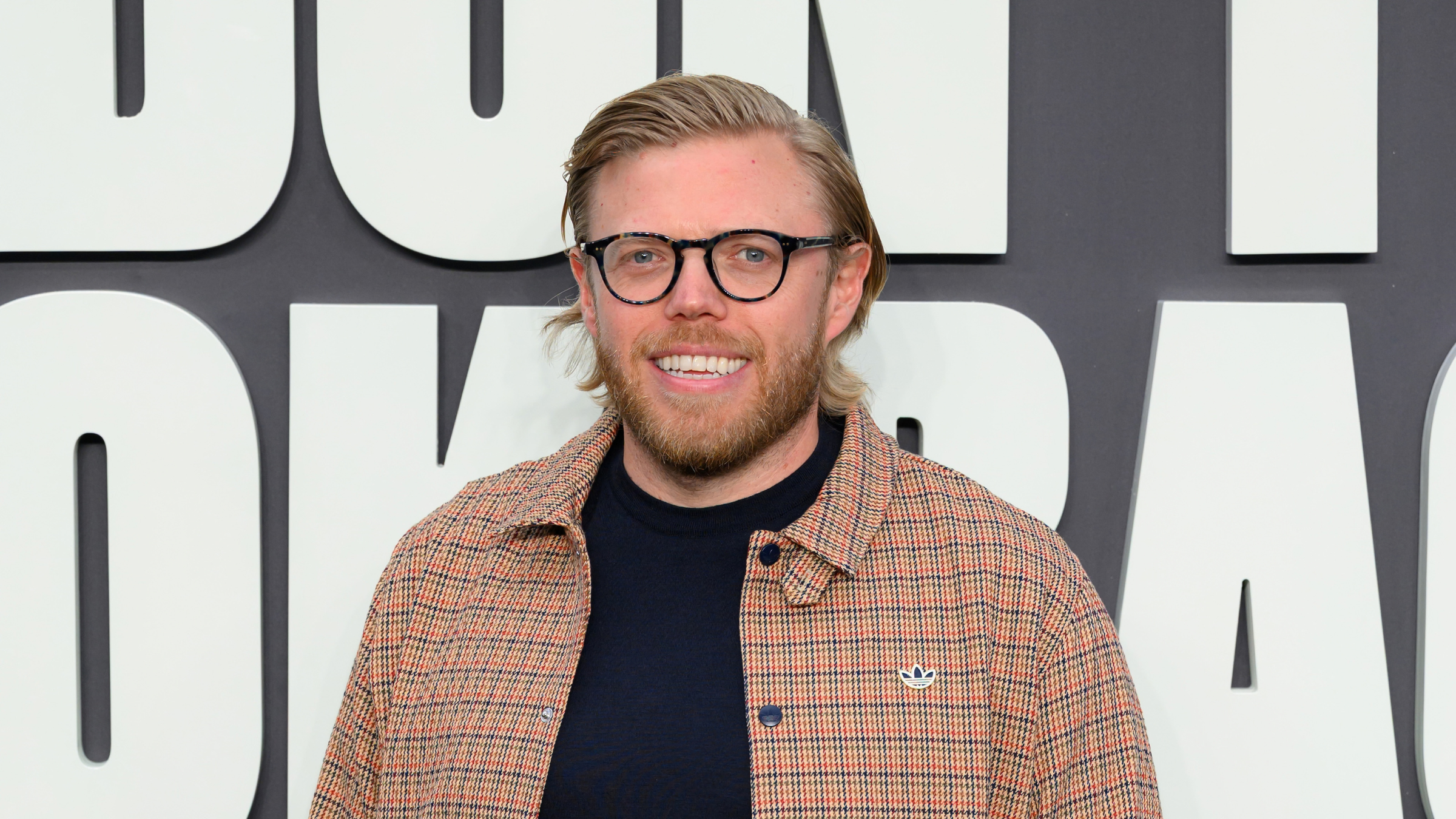 Rob Beckett in beige check shirt and black t-shirt at Oasis Don't Look Back In Anger premier.