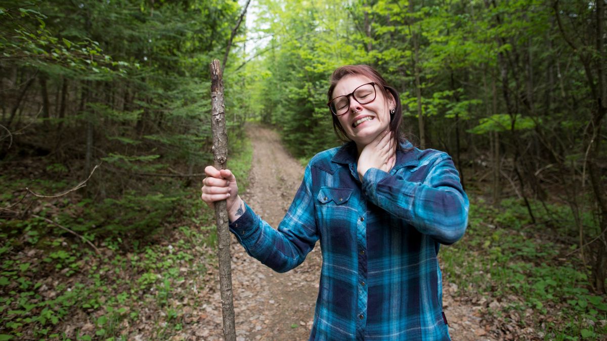 woman winces in discomfort as she is slapping her neck to kill a bug that is biting her