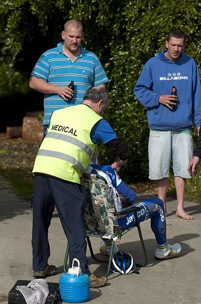 Medical officer Bobby Hall attends to an injured rider as some spectators enjoy a beer.