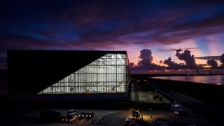 a large building with big, lit-up windows sits beneath a darkening sunset sky