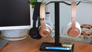 Avantree dual headphone stand resting on a desk with two headphones attached to it.