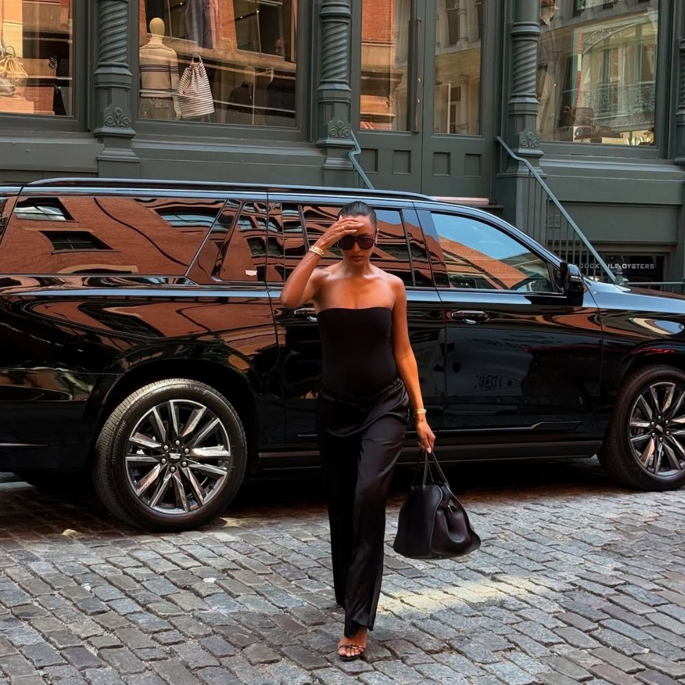 Model Jasmine Tookes wears black satin trousers with a black strapless top and black The Row Margaux bag.