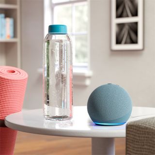 Blue round Amazon Echo Dot (4th Gen) next to water bottle on white side table