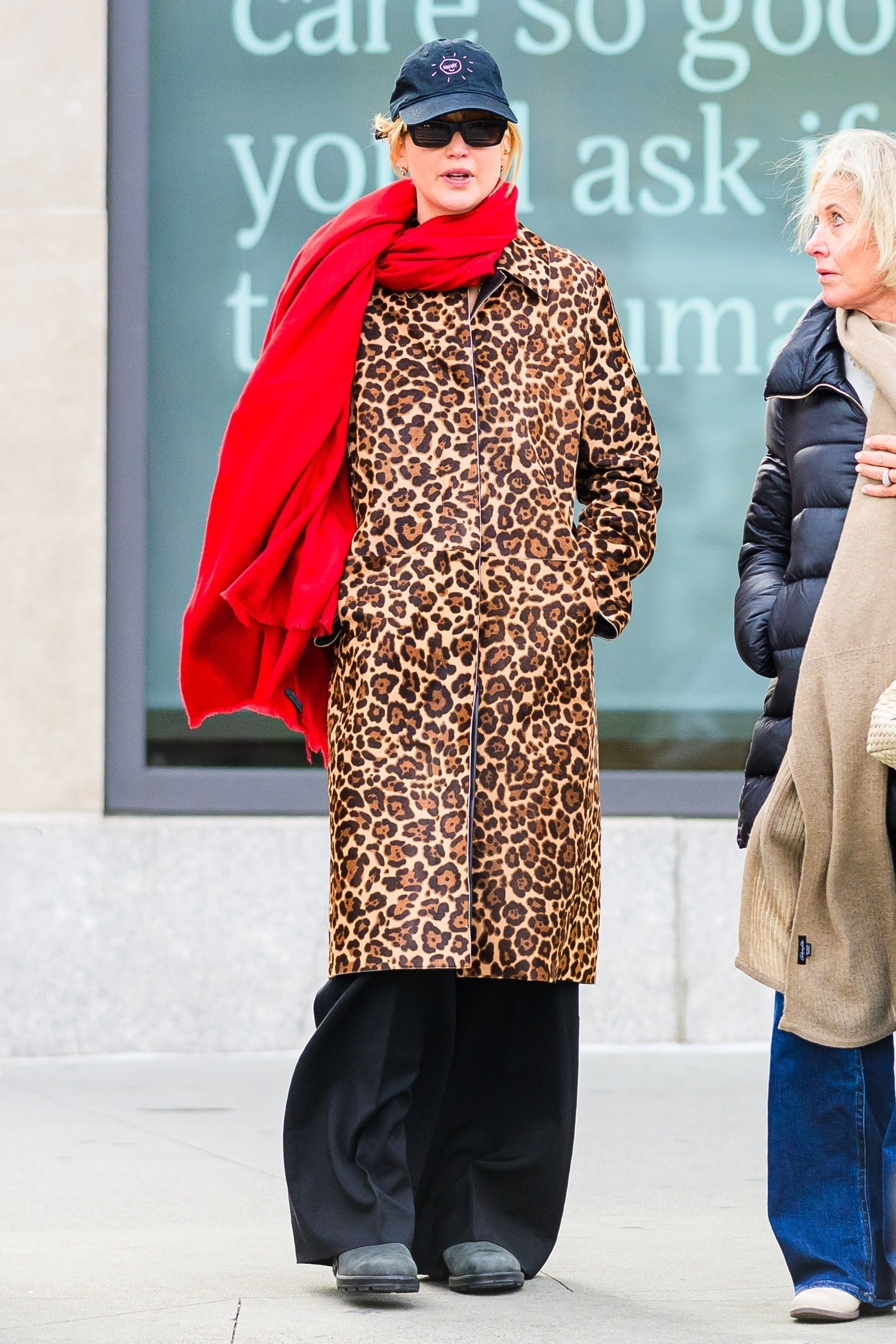 Jennifer Lawrence wears a baseball cap, red scarf, leopard-print coat, blundstone clogs, and black trousers.