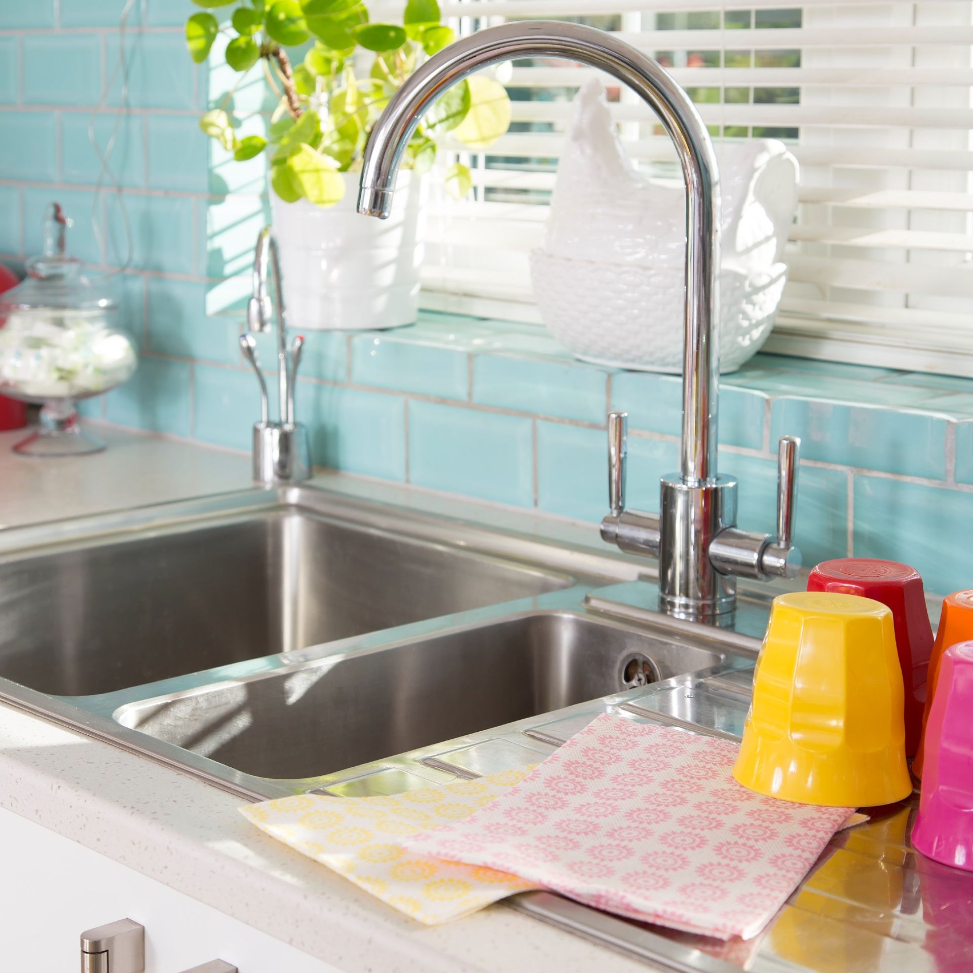 A steel kitchen sink with colourful cups drying next to it