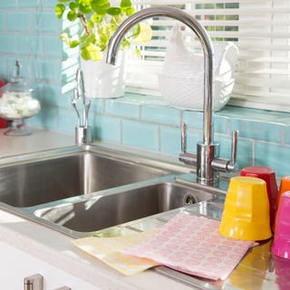 A steel kitchen sink with colourful cups drying next to it