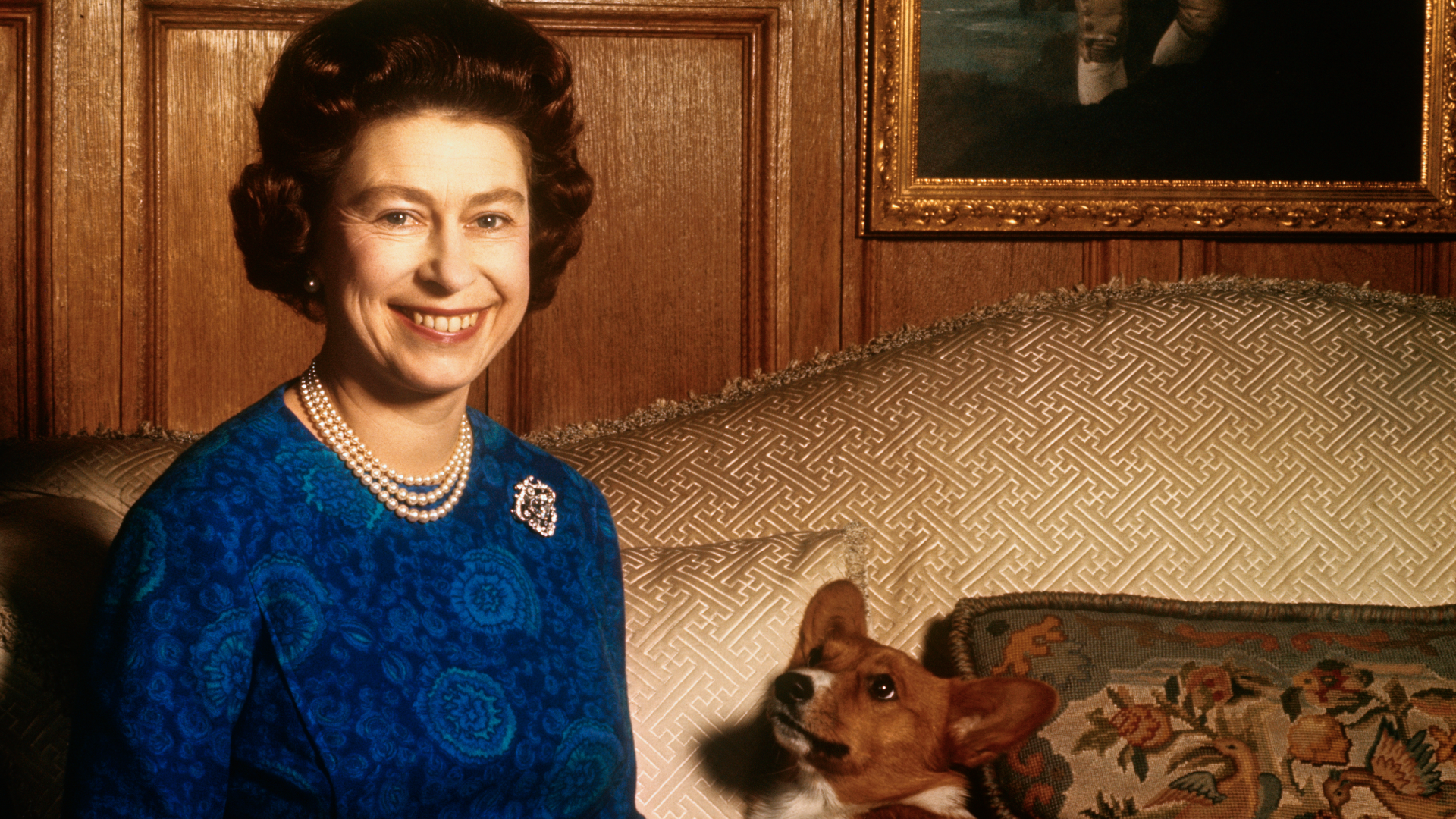 Queen Elizabeth sitting on a sofa with a corgi