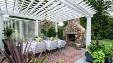 A pergola and trellis in white in an outdoor dining area with fireplace
