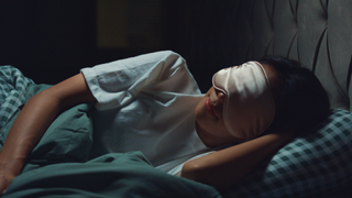 Woman wearing eye mask sleeping in bed